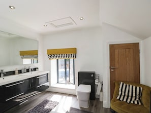 A modern bathroom with a large mirror, a black vanity, a toilet, and a window with a yellow and black valance. - Llanfarach Farmhouse (Pontyclun)