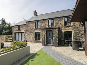 A stone house with a paved patio, a door, and a small garden area. - Llanfarach Farmhouse (Pontyclun)