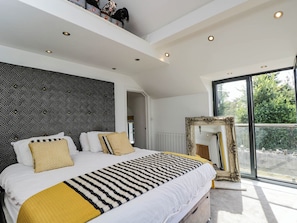 A bedroom with a large bed, a patterned headboard, and a view through a large window. - Llanfarach Farmhouse (Pontyclun)