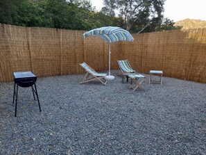 A backyard with a bamboo fence, a gravel ground, and a striped umbrella.