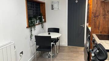 A compact kitchen with a dining table, chairs, a clock, and a door.