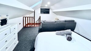 Una camera da letto moderna con un letto, una cassettiera, un angolo salotto e una scala.
