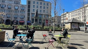Zona esterna con tavoli e sedie, circondata da edifici e una statua.