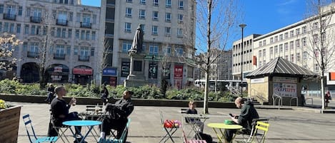 An outdoor seating area with tables and chairs, surrounded by buildings and a statue.