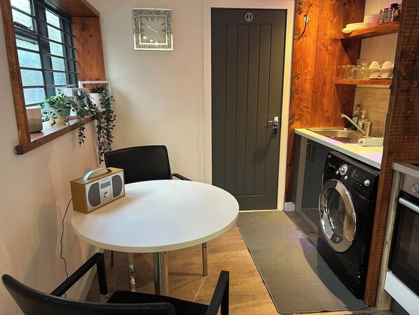 A compact kitchen with a washing machine, a sink, and a dining area with a table and chairs.