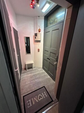 A narrow hallway with a bench, a door, and a wall-mounted air conditioning unit.