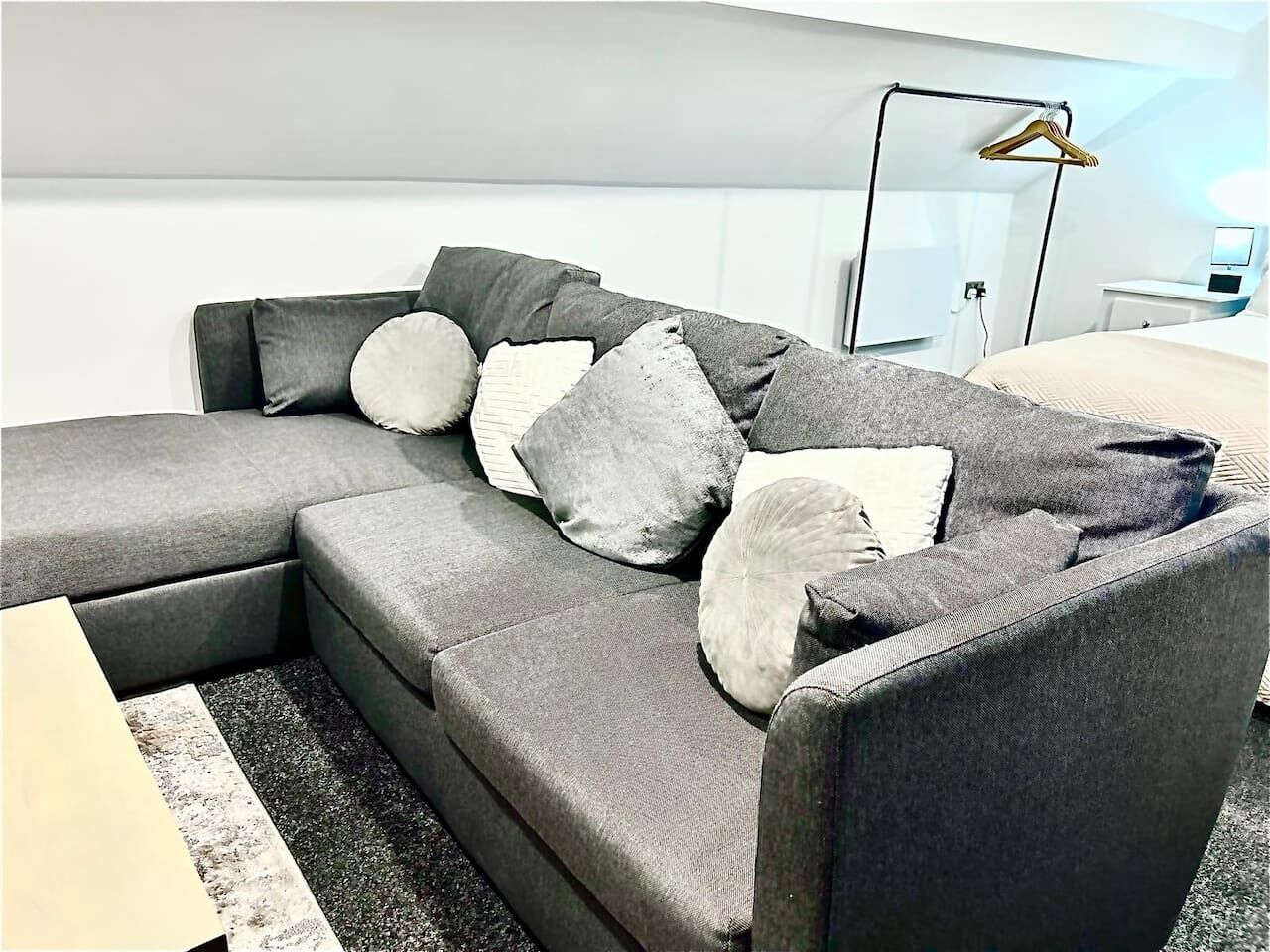 A modern living room with a grey sectional sofa, multiple cushions, a black floor lamp, and a white wall.