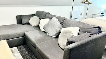 A modern living room with a grey sectional sofa, multiple cushions, a black floor lamp, and a white wall.