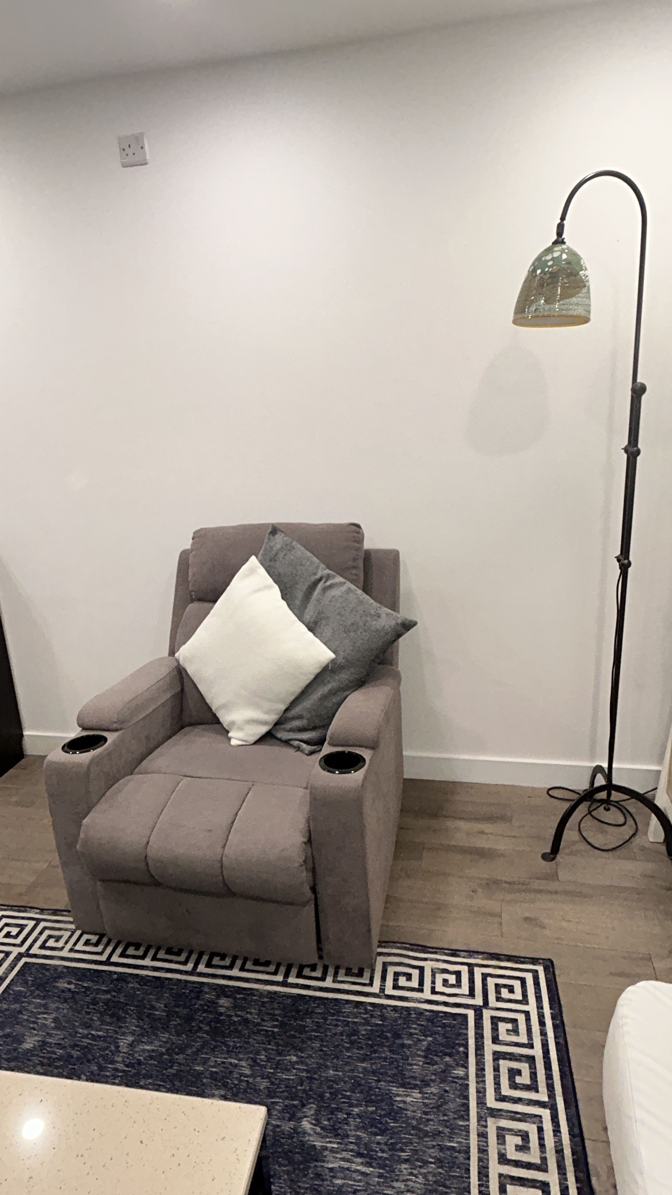 Quarto com poltrona reclinável, luminária de chão e tapete estampado.