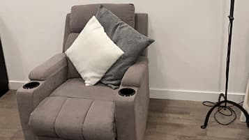Quarto com poltrona reclinável, luminária de chão e tapete estampado.