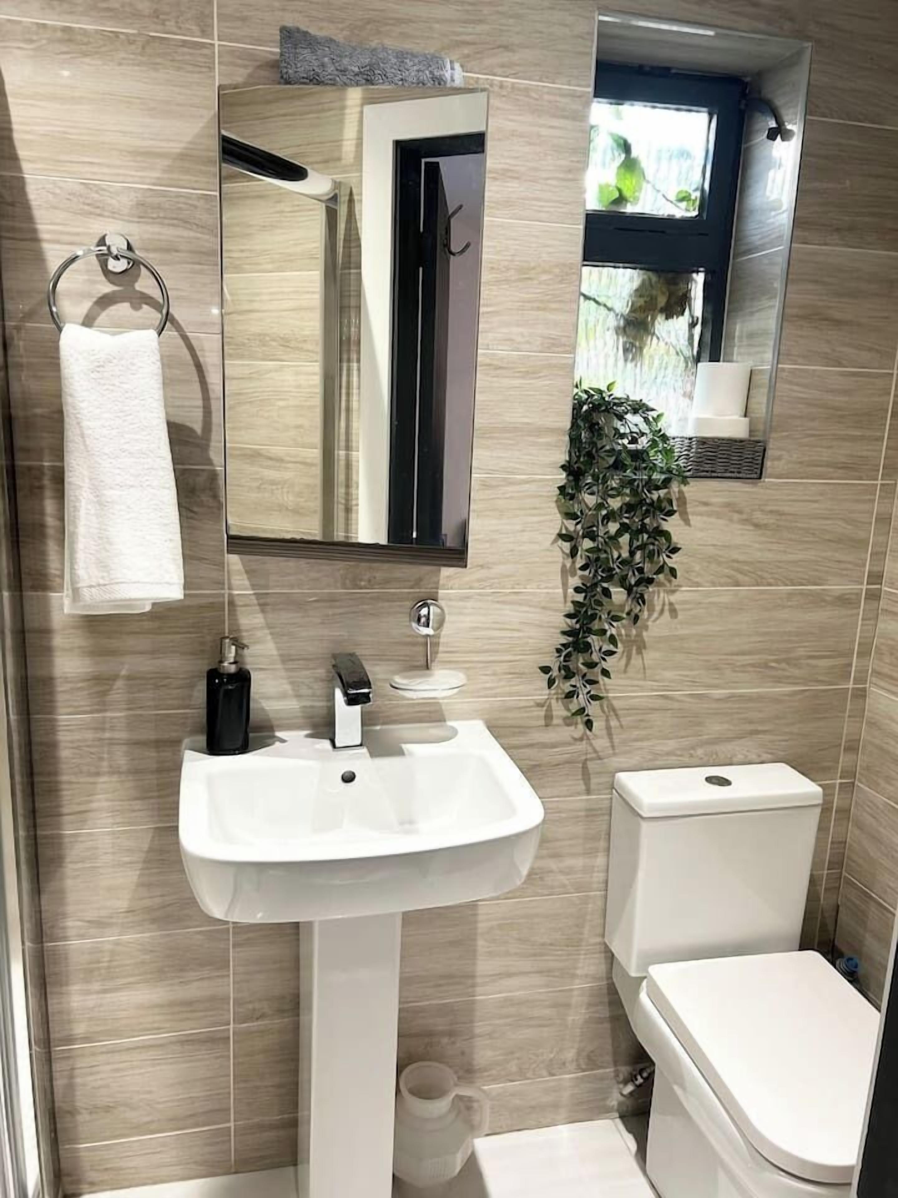 Ein Badezimmer mit weißem Waschbecken, Toilette, Spiegel und Handtuchhalter.