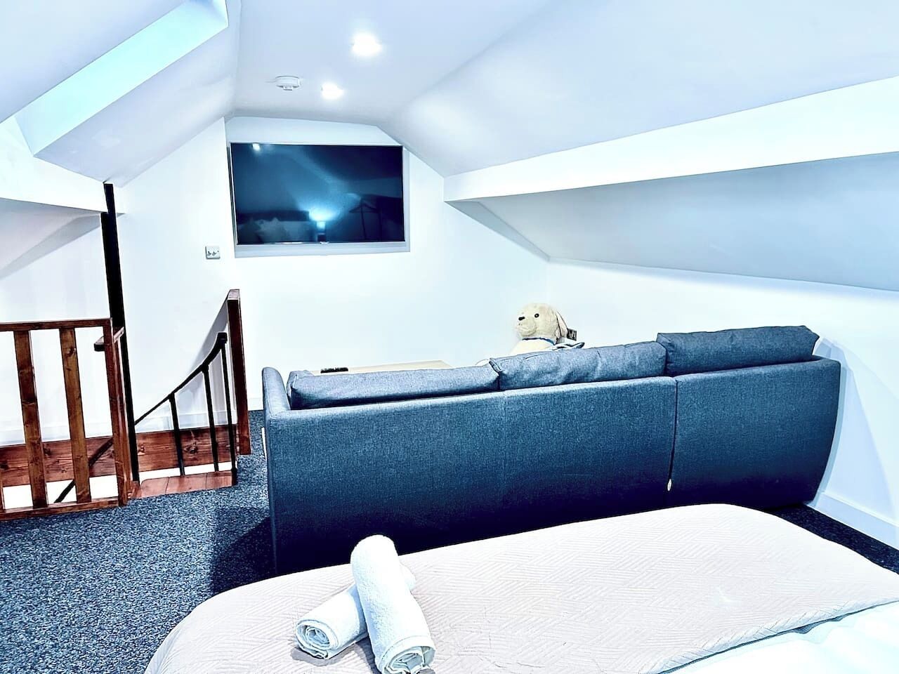 A modern room with a sofa, a bed, a TV mounted on the wall, and a staircase.