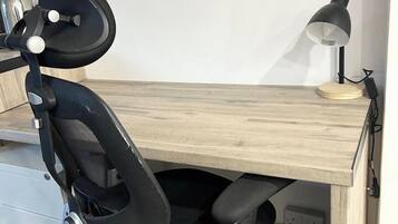A wooden desk with a black office chair, a lamp, and a power outlet.