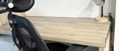 A wooden desk with a black office chair, a lamp, and a power outlet.