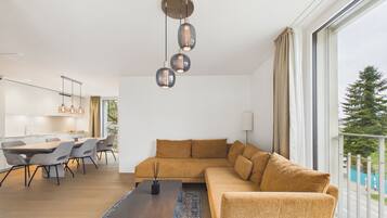 Ein modernes Wohnzimmer mit einer großen Couch, einem Essbereich mit Tisch und Stühlen sowie einer Küche im Hintergrund.