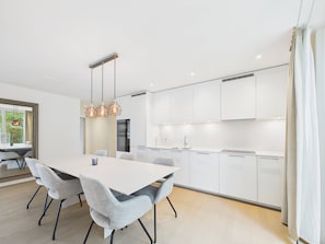 Cozinha moderna com armários brancos, ilha central e iluminação pendente.