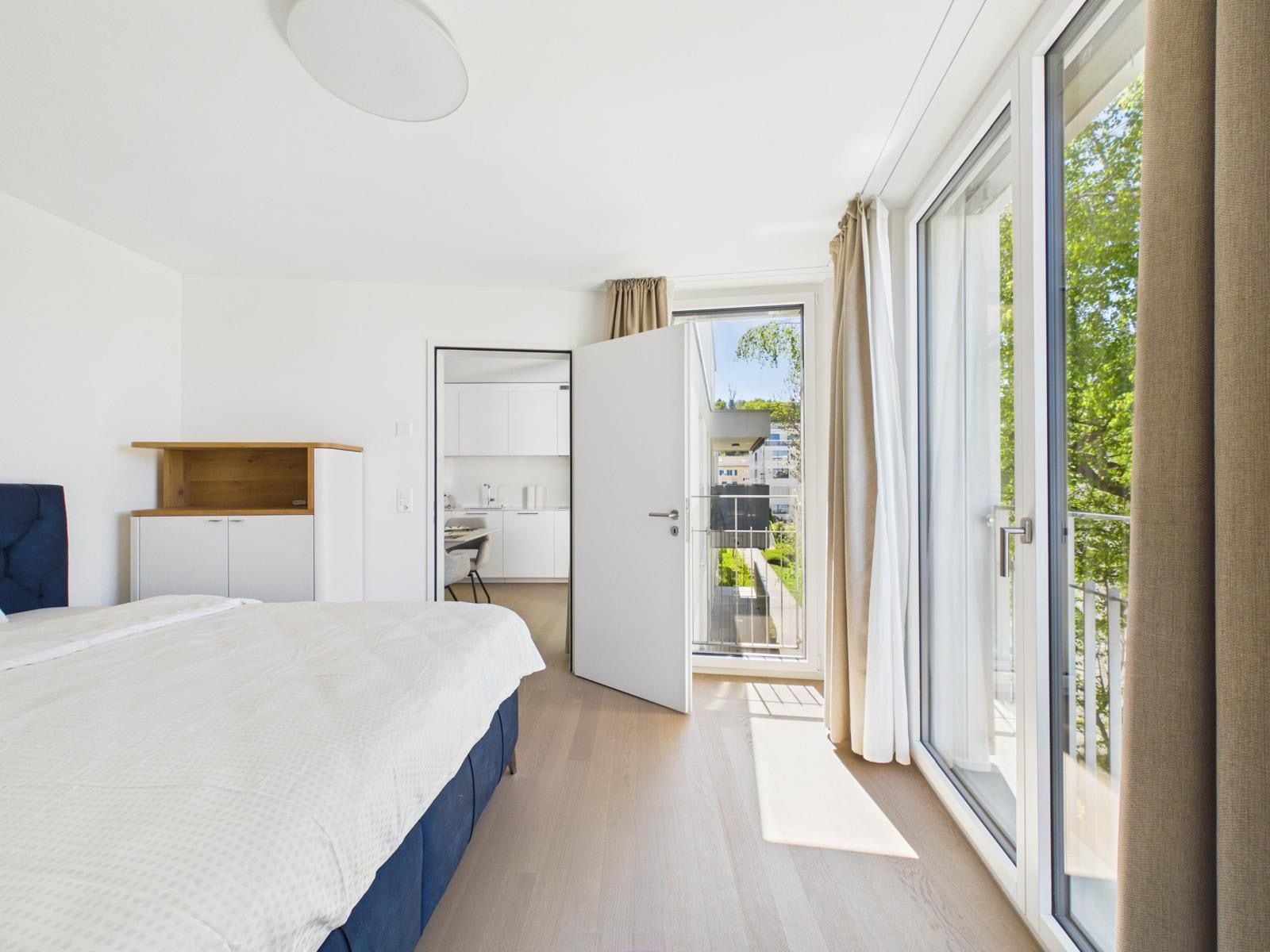 Un dormitorio con cama, escritorio, armario y balcón con vistas.