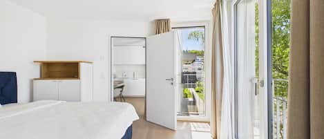 A bedroom with a bed, a desk, a wardrobe, and a balcony with a view.