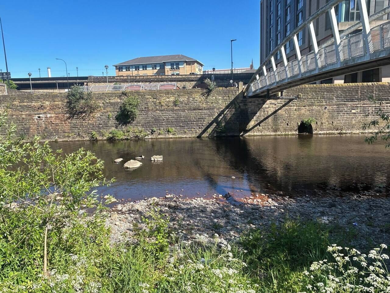 Une rivière avec un pont, un mur de pierre et un bâtiment en arrière-plan.
