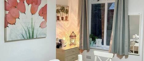 A dining area with a table set for four, a painting on the wall, and a window with curtains.