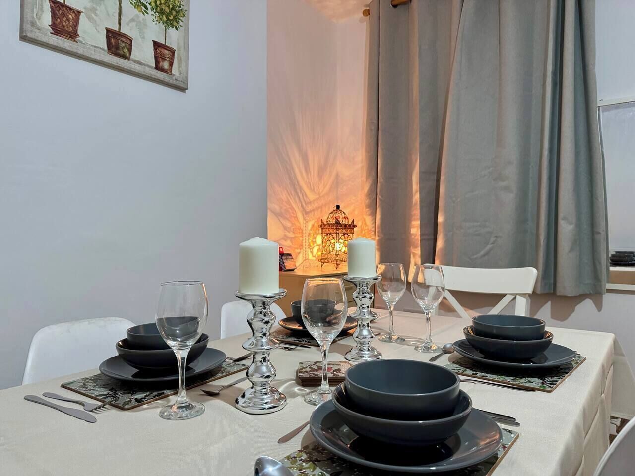 A dining table set with black plates, glasses, and candles, with a candle holder and a framed picture on the wall.