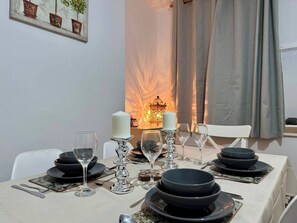 A dining table set with black plates, glasses, and candles, with a candle holder and a framed picture on the wall.