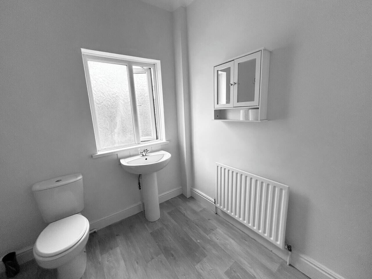 Ein Badezimmer mit Toilette, Waschbecken, Fenster und einem weißen Heizkörper.
