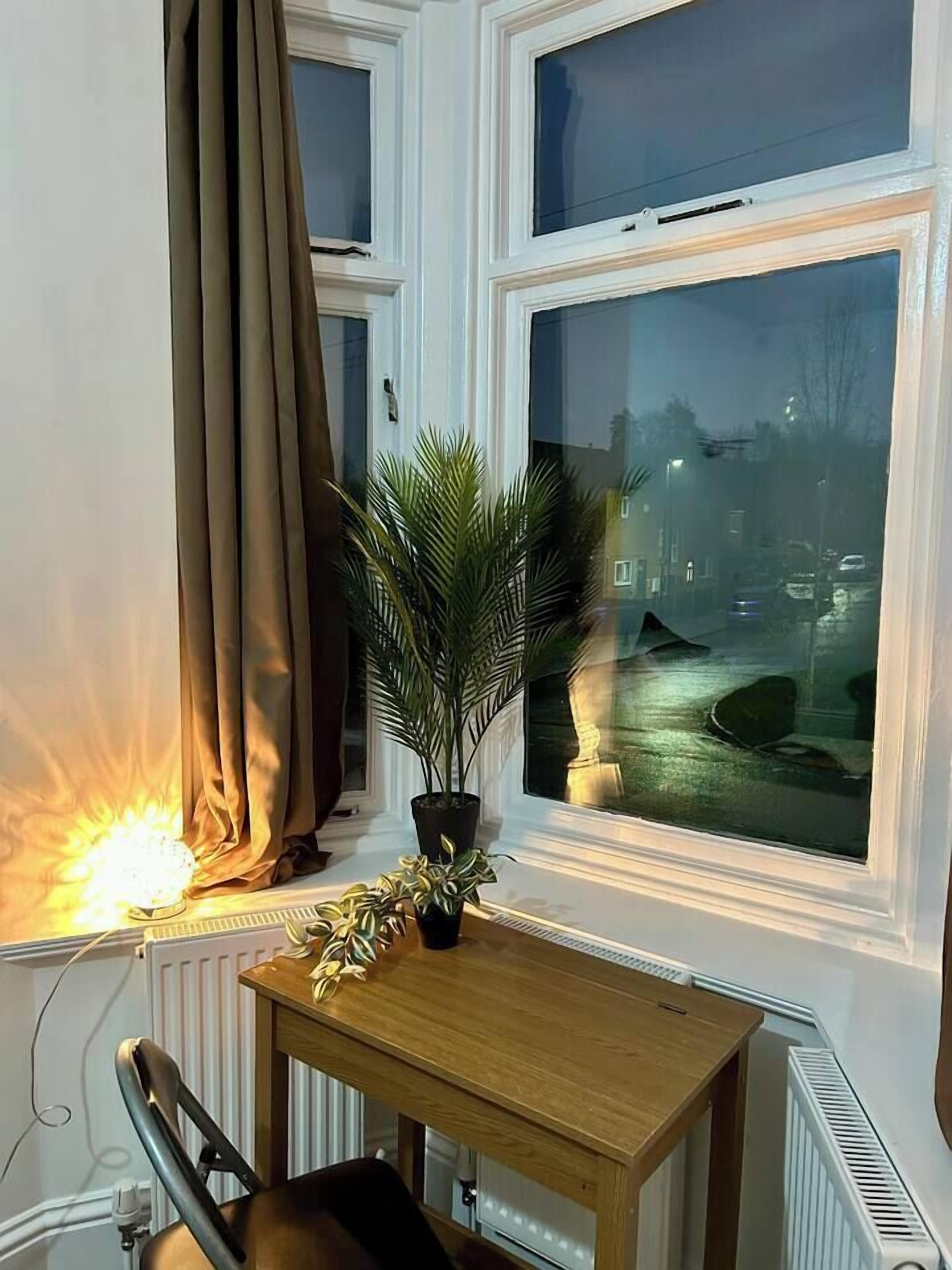 A room with a large window, a table, a chair, and a potted plant.