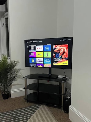 Een flatscreen televisie bevestigd aan een zwarte standaard, met een afstandsbediening op een klein tafeltje.