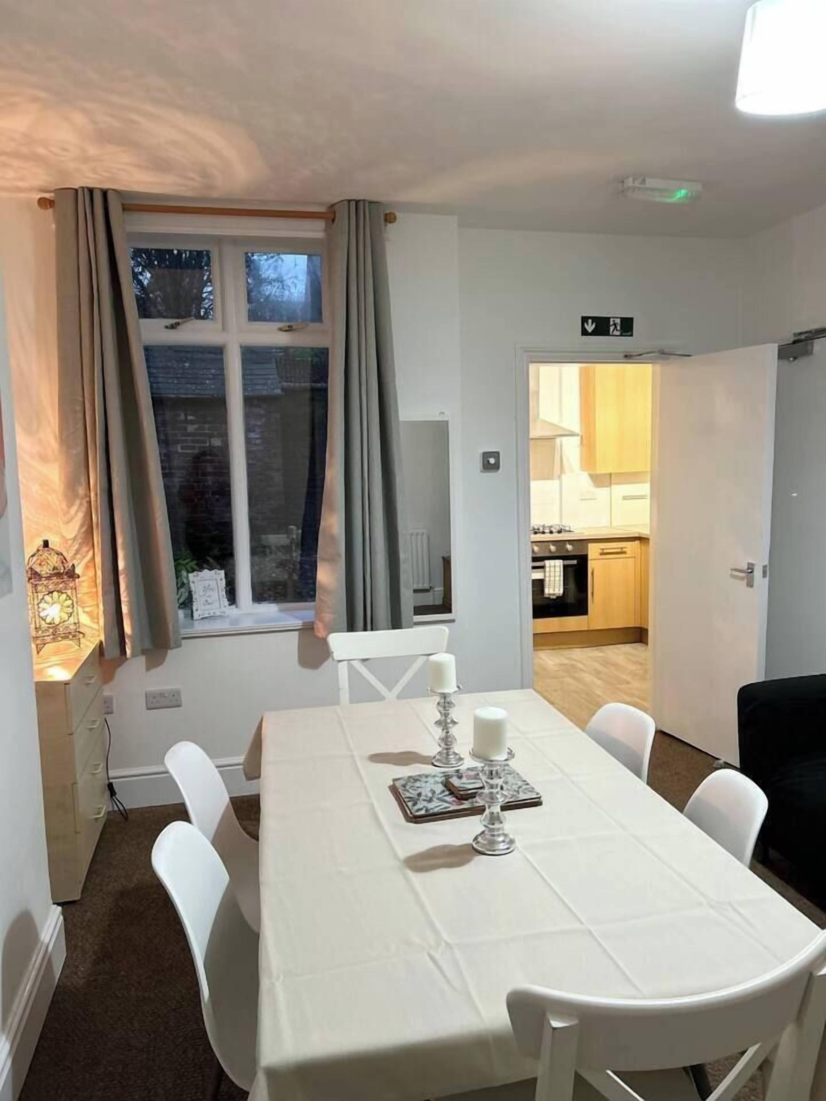 A dining area with a table set for four, a window with curtains, and a view into a kitchen.