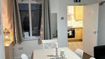 A dining area with a table set for four, a window with curtains, and a view into a kitchen.