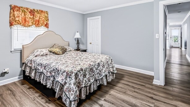 A bedroom with a bed, a nightstand, a lamp, and a window with a floral curtain. - Charming Single-Family Home (Greenville)