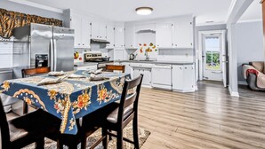 A modern kitchen with white cabinets, a stainless steel refrigerator, and a dining area with a table set for four. - Charming Single-Family Home (Greenville)