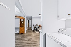 A laundry room with a white washing machine, a wooden cabinet, and a dining area with chairs and a table.