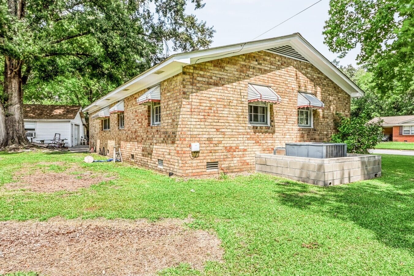 Una casa a un piano in mattoni con un portico coperto, un piccolo garage annesso e un prato ben curato.
