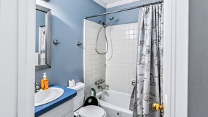 A bathroom with a bathtub, toilet, sink, and a shower curtain with a pattern. - Charming Single-Family Home (Greenville)