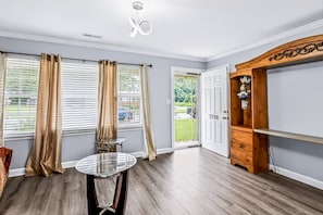 A room with a wooden floor, a glass table, curtains, a door with a number, and a cabinet.