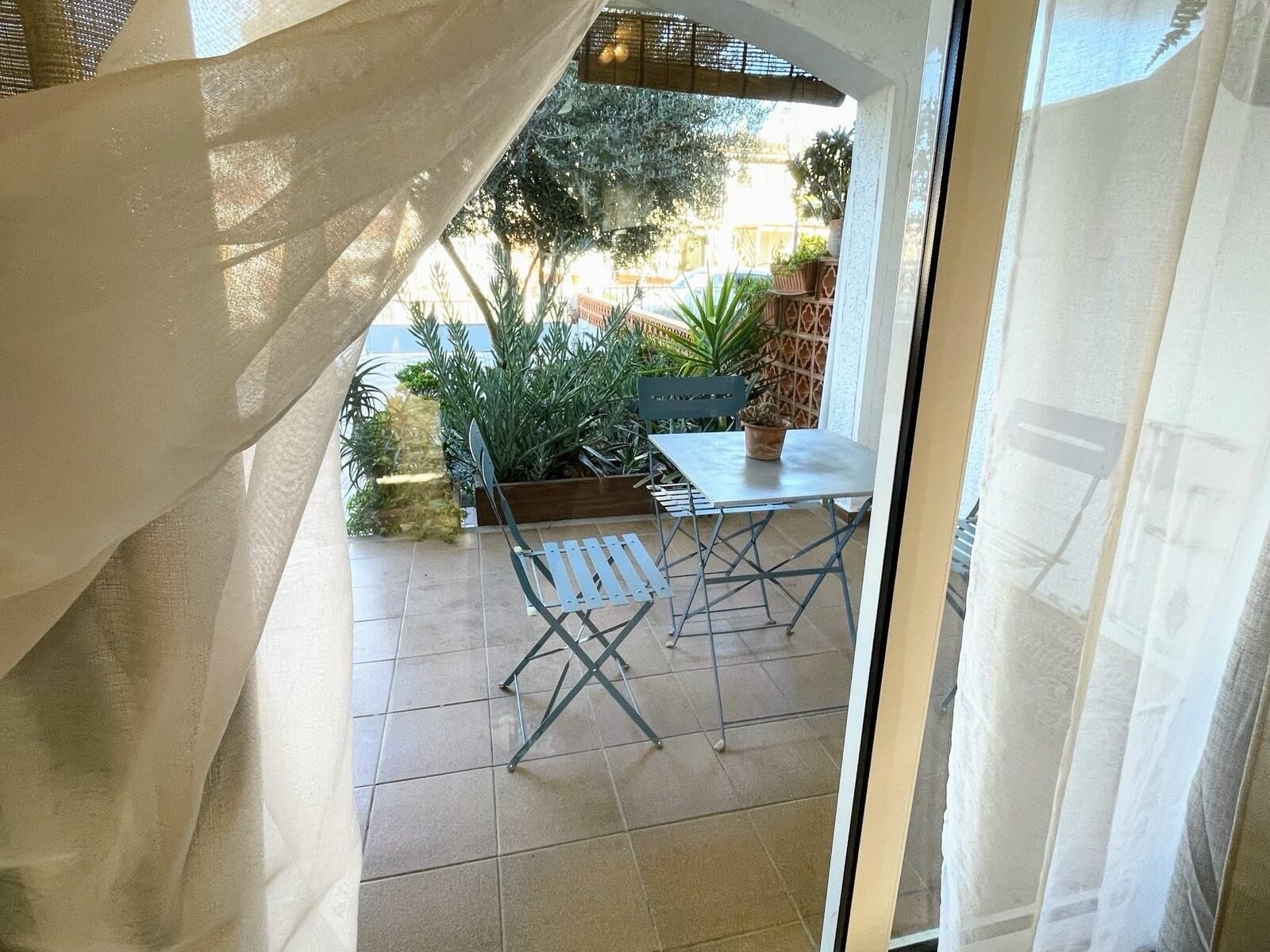 Un espace extérieur aménagé en patio, avec une table et des chaises, entouré de plantes en pot et d’une clôture en bois.
