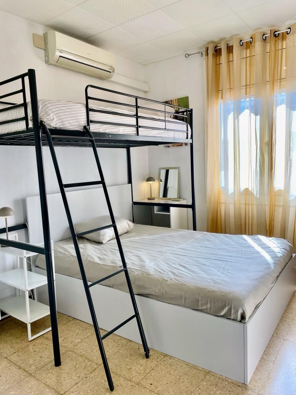 A bunk bed room with a ladder, a desk, a chair, and a window with curtains.