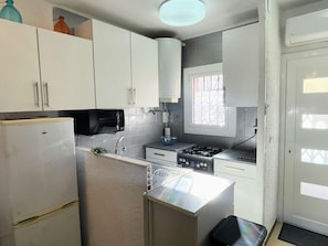 Una cocina pequeña con gabinetes blancos, un microondas negro, una estufa y un lavamanos.