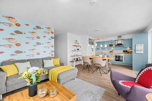 Un salon moderne avec un canapé, une table basse et un mur décoré d’une fresque colorée représentant des poissons.