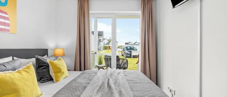A hotel room with a bed, a TV, and a view of the outside.