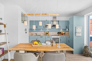 Une cuisine moderne avec des meubles bleus, une table à manger en bois et des luminaires suspendus.
