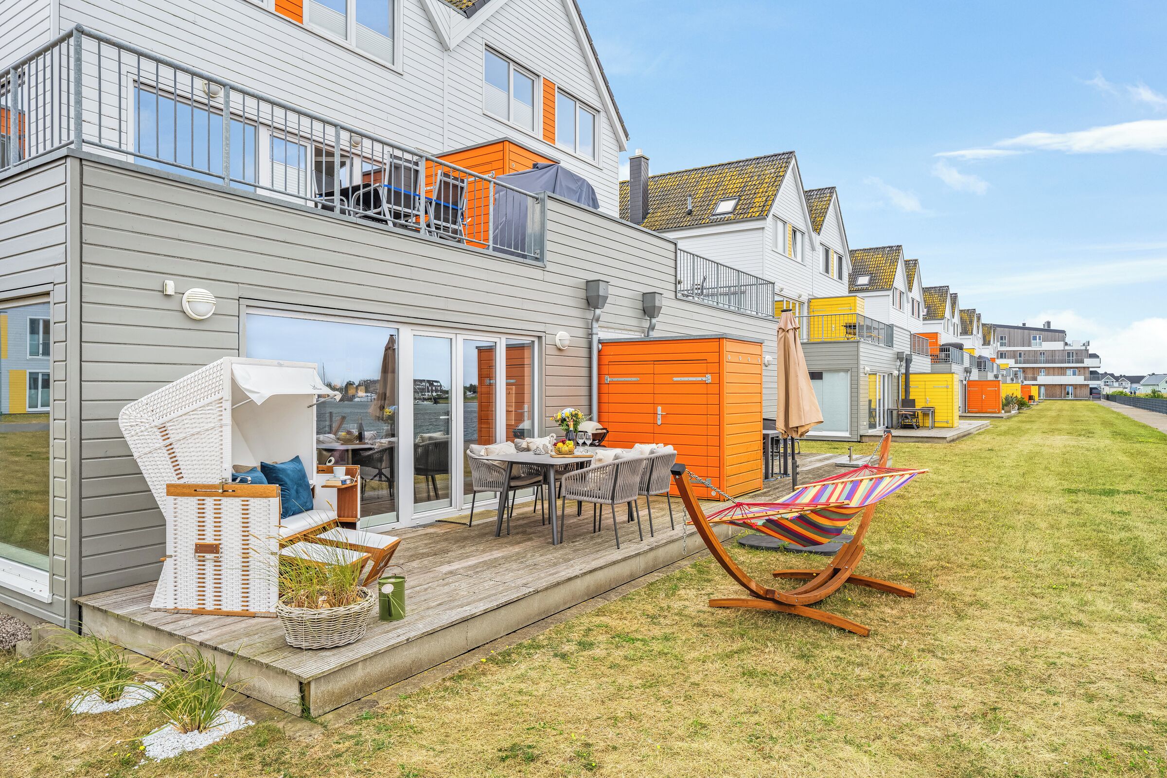 Ein modernes, zweistöckiges Haus mit einer Terrasse, Gartenmöbeln und einer Hängematte.