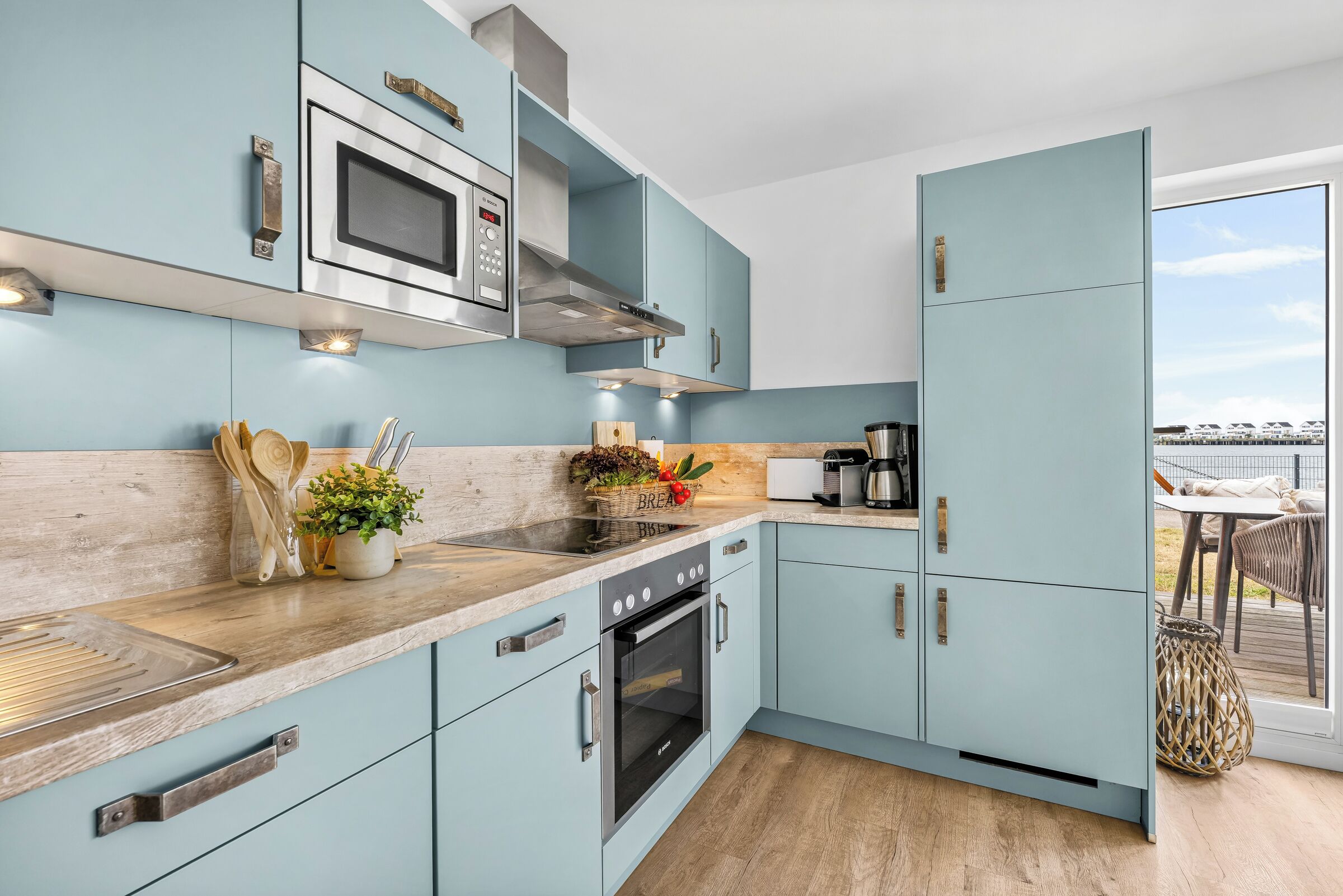 A modern kitchen with light blue cabinets, stainless steel appliances, and a wooden countertop.