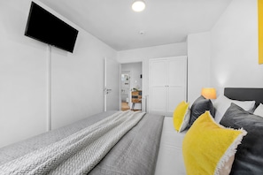 A modern bedroom with a bed, bedside table, lamp, and a TV mounted on the wall. - Fischerman's Friend - First row on the waterfront, infrared sauna, 3 TVs, close to the beach (Olpenitz)