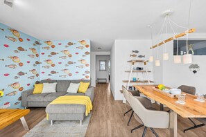 Un salon moderne avec un canapé gris, un plaid jaune et un mur décoré d’un motif de poissons bleus.