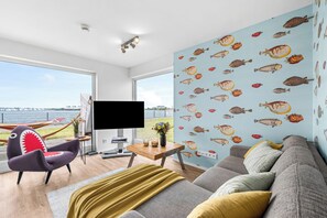 A modern living room with a large window, a flat-screen TV, a sofa, a chair, and a wall with fish decals. - Fischerman's Friend - First row on the waterfront, infrared sauna, 3 TVs, close to the beach (Olpenitz)