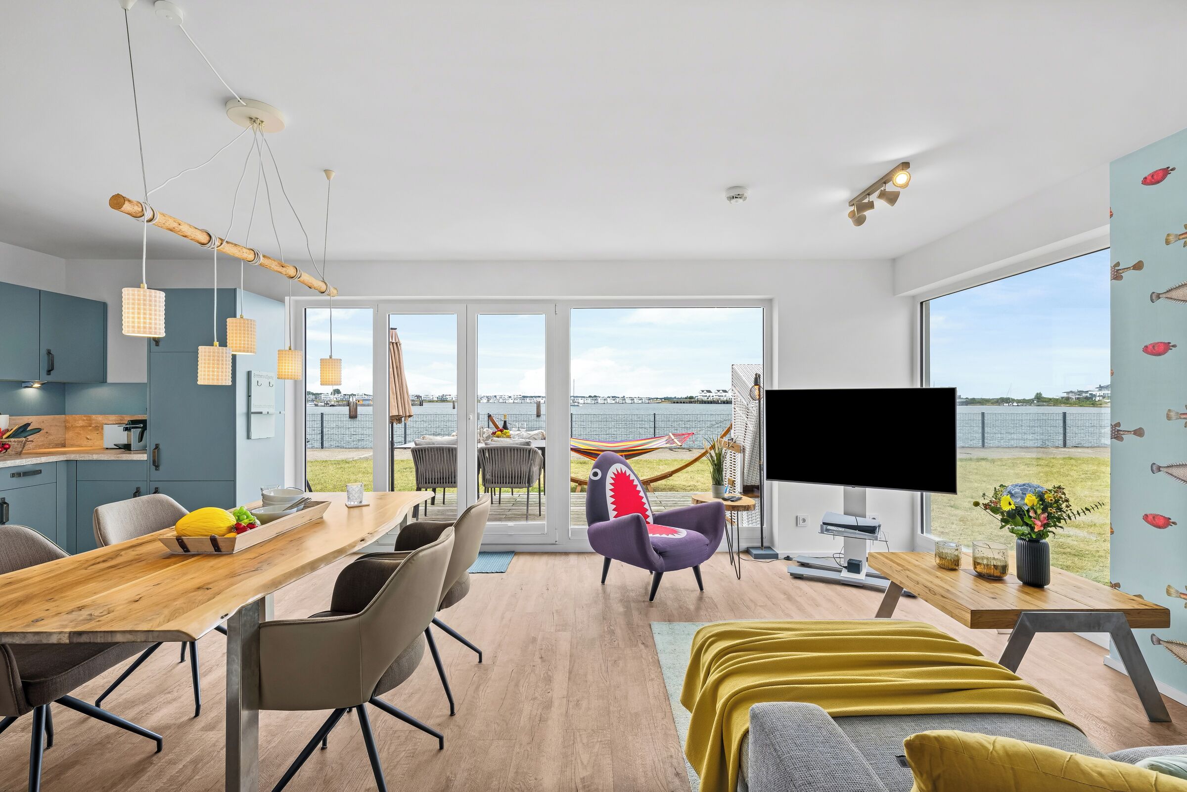 A modern living room with a large window, a flat-screen TV, and a dining area with a wooden table and chairs.
