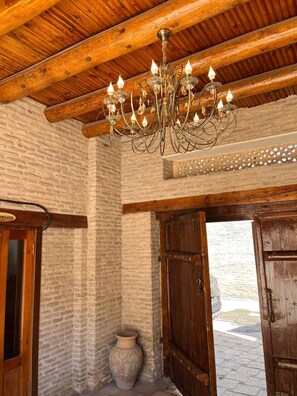 A room with a wooden ceiling, a brick wall, and a chandelier. There is a wooden door and a large vase on the floor.